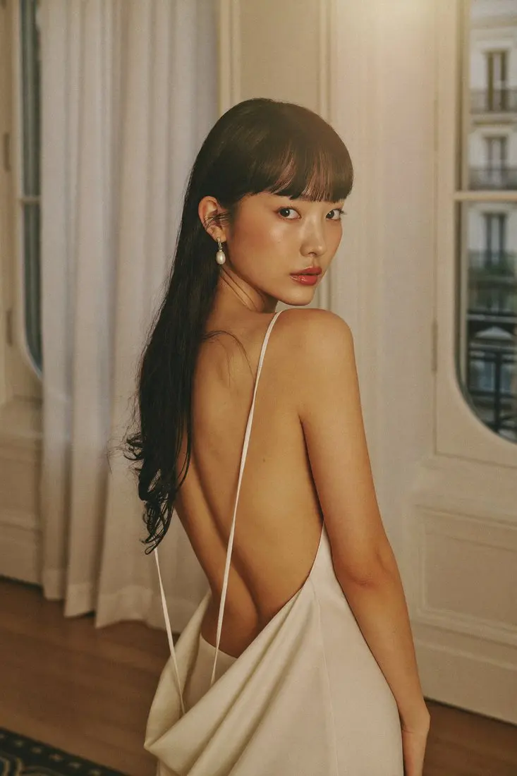 Before: model in a white backless dress by a Paris window
