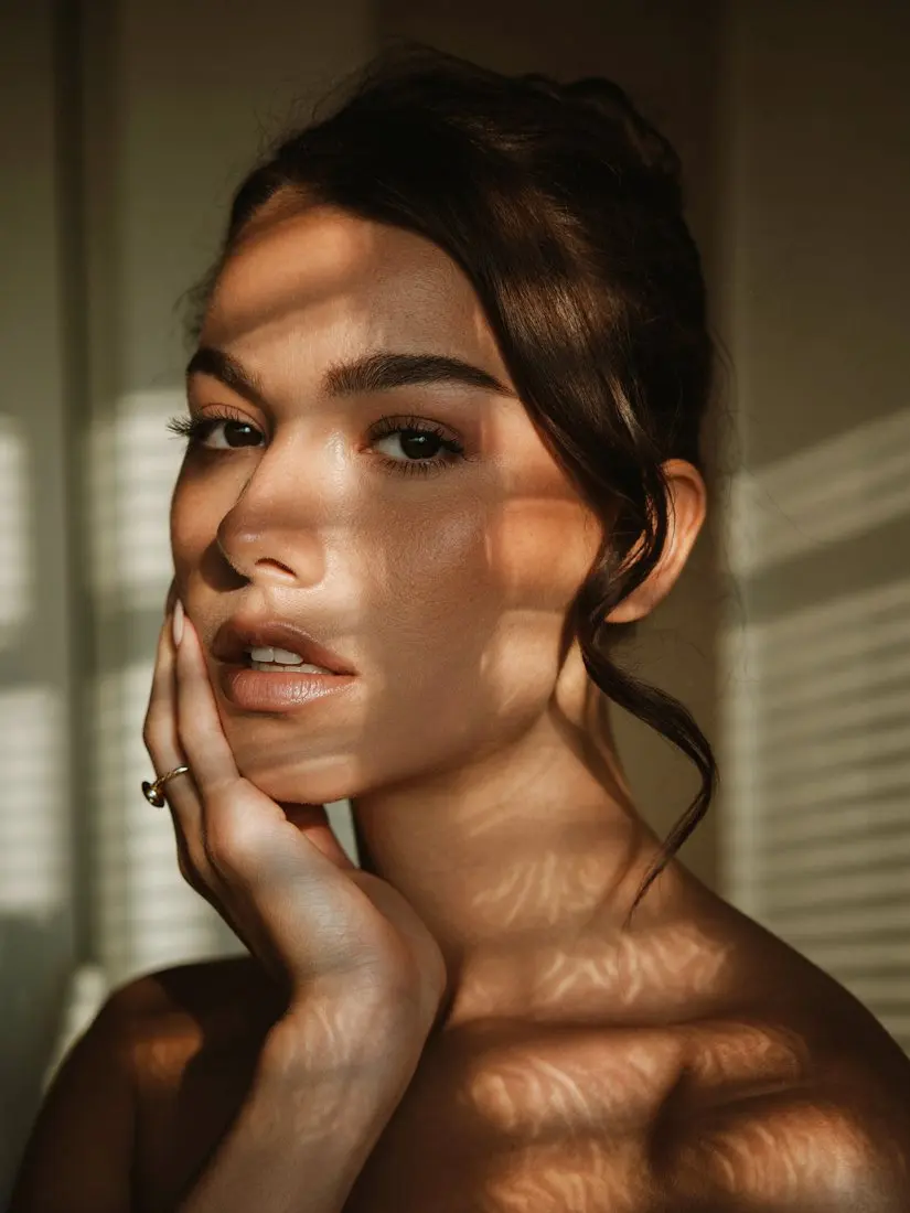 Before: person with a hand on their cheek in striped window light, face and hair as photographed